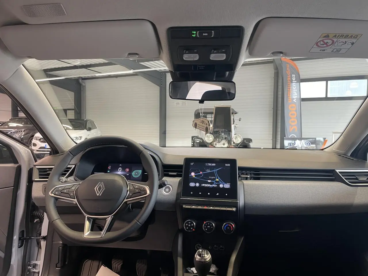 Vue intérieure frontale de la Renault Clio 2025, tableau de bord gris avec écran tactile 7 pouces et volant multifonction.