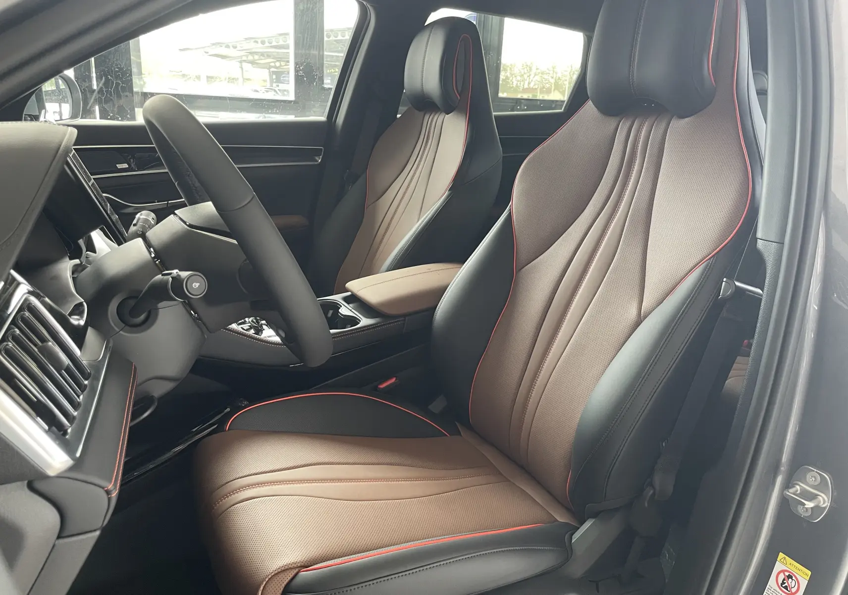 Vue intérieure côté conducteur du BYD SEAL U 2025 avec sièges en similicuir vegan noir et brun à surpiqûres rouges.