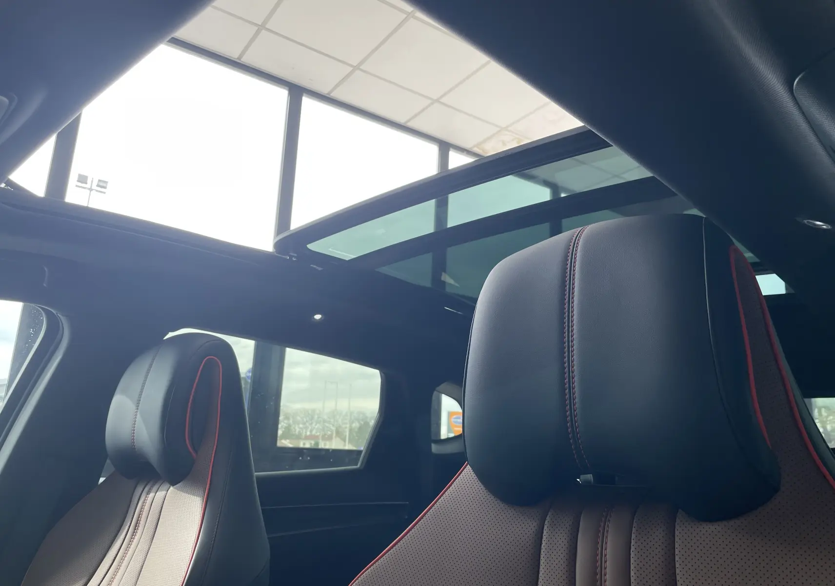 Vue intérieure rapprochée des sièges avant noirs avec surpiqûres rouges et toit ouvrant panoramique du BYD SEAL U gris.