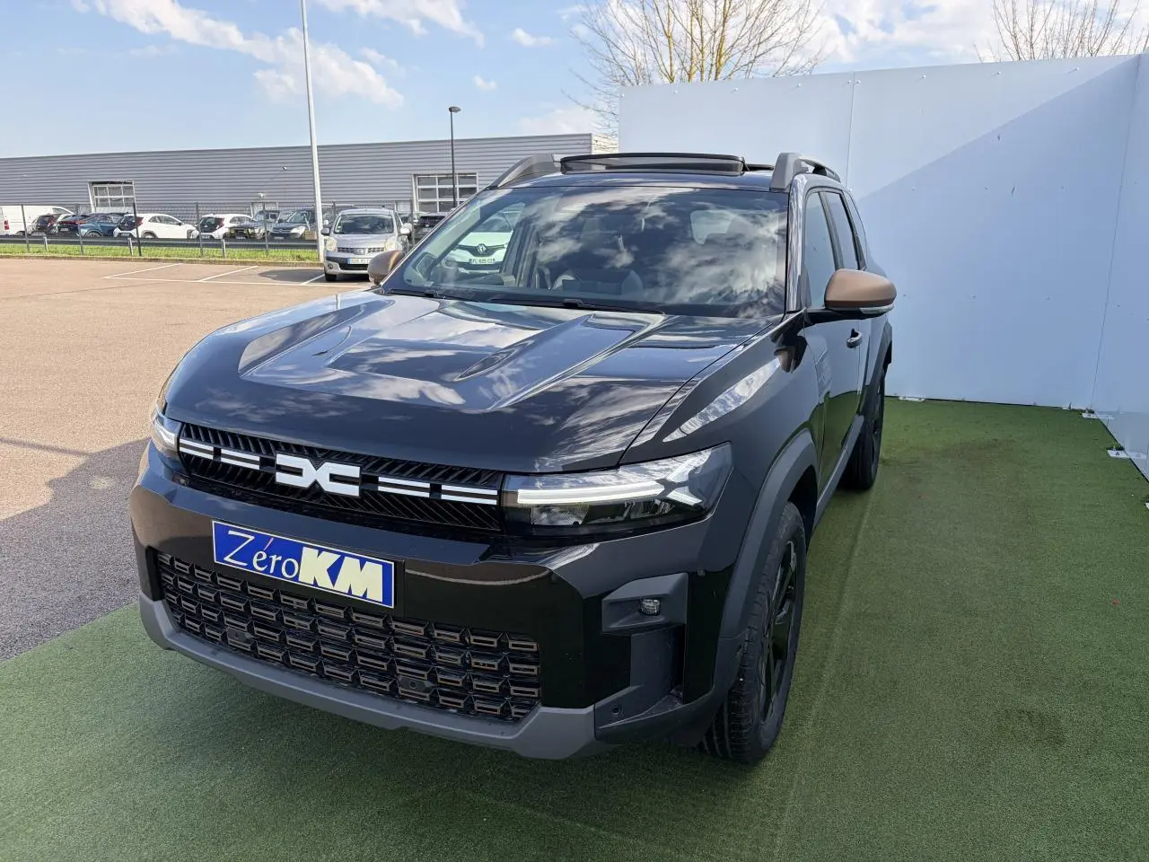 Vue 3/4 avant du Dacia Bigster noir nacré avec calandre et rétroviseurs brun cuivré, toit panoramique ouvert.