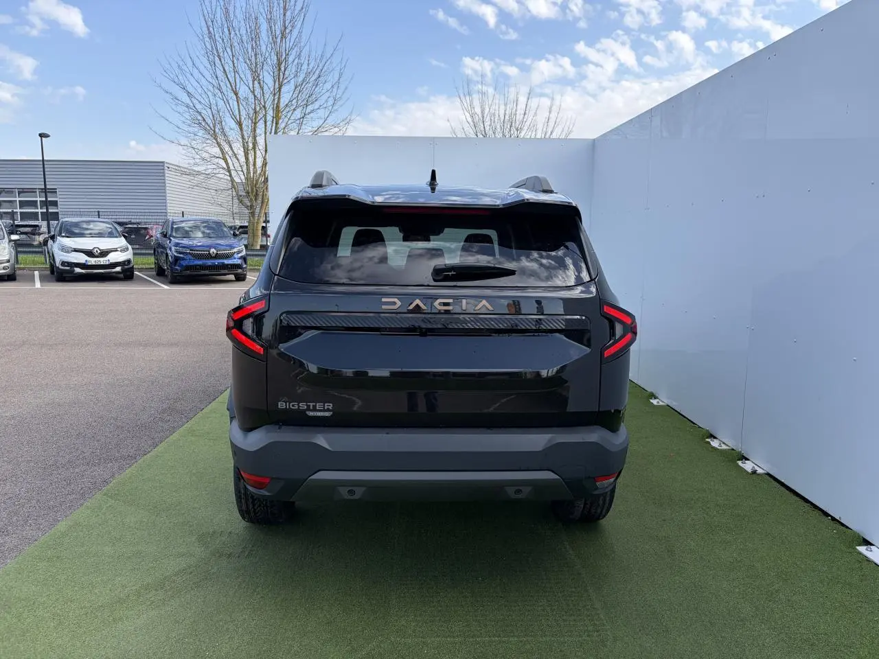 Vue arrière d'un Dacia Bigster noir nacré avec feux LED en forme de C et logo Dacia brun cuivré visible.