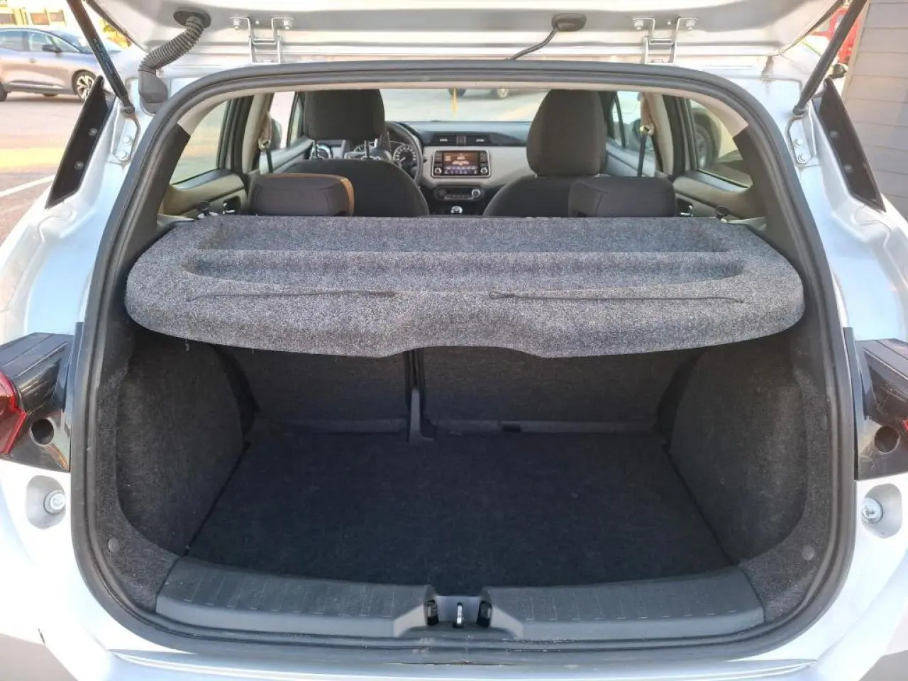 Vue arrière du coffre ouvert d'une Nissan Micra gris clair 2022, avec cache-bagages et intérieur noir visible.