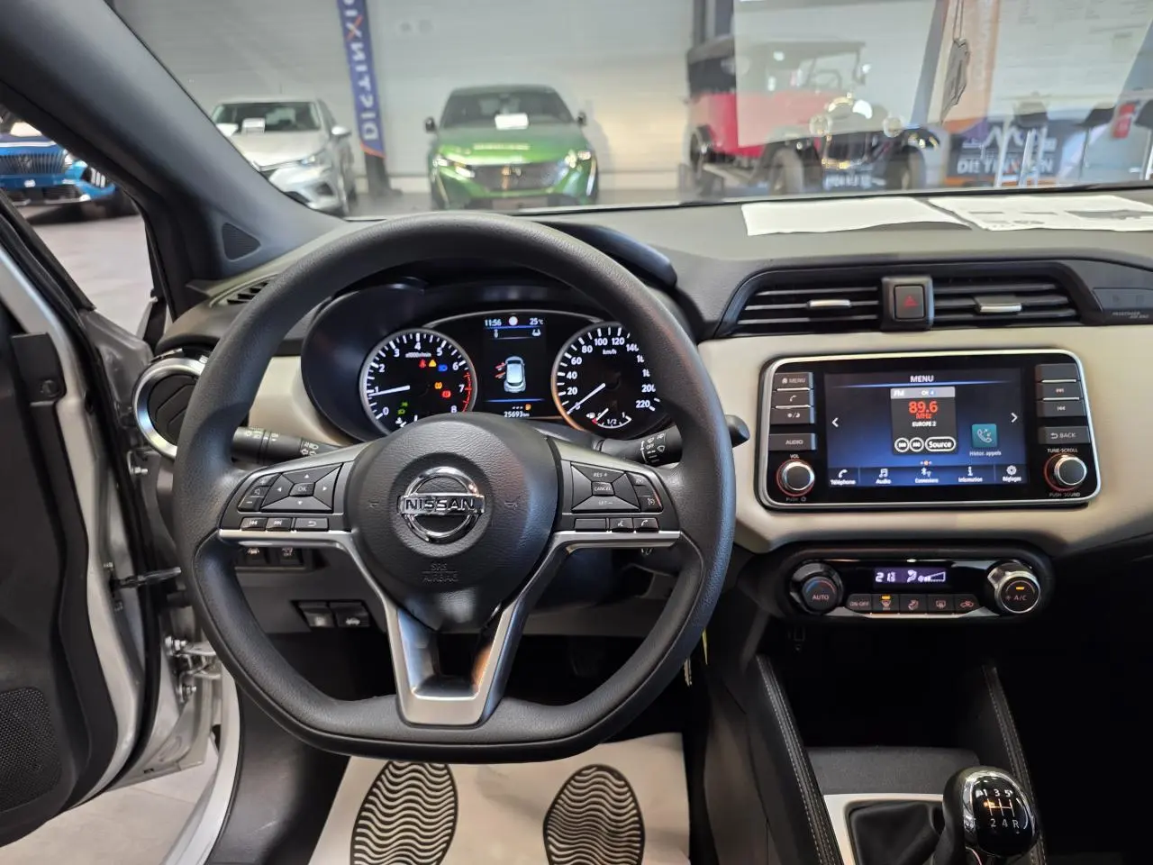 Vue intérieure avant centrée sur le volant Nissan Micra gris clair avec tableau de bord beige et écran tactile 7 pouces.