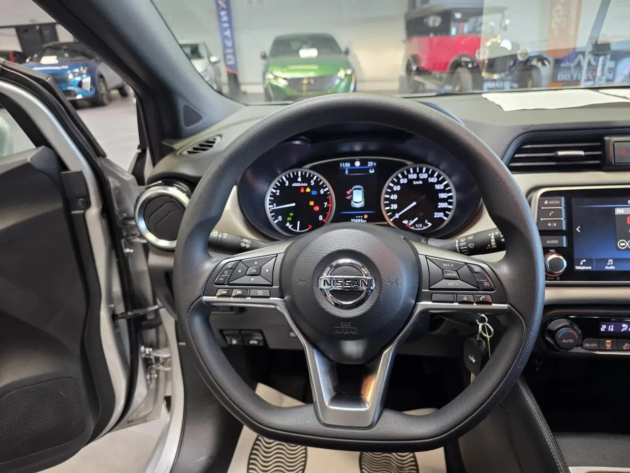 Vue intérieure centrée sur le volant noir de la Nissan Micra gris clair avec tableau de bord et écran tactile visible.