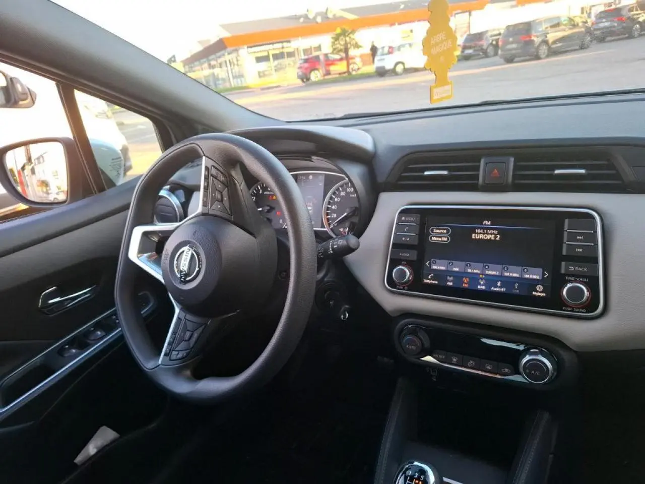 Vue intérieure côté conducteur de la Nissan Micra 2022, tableau de bord beige avec écran tactile et volant multifonction noir.