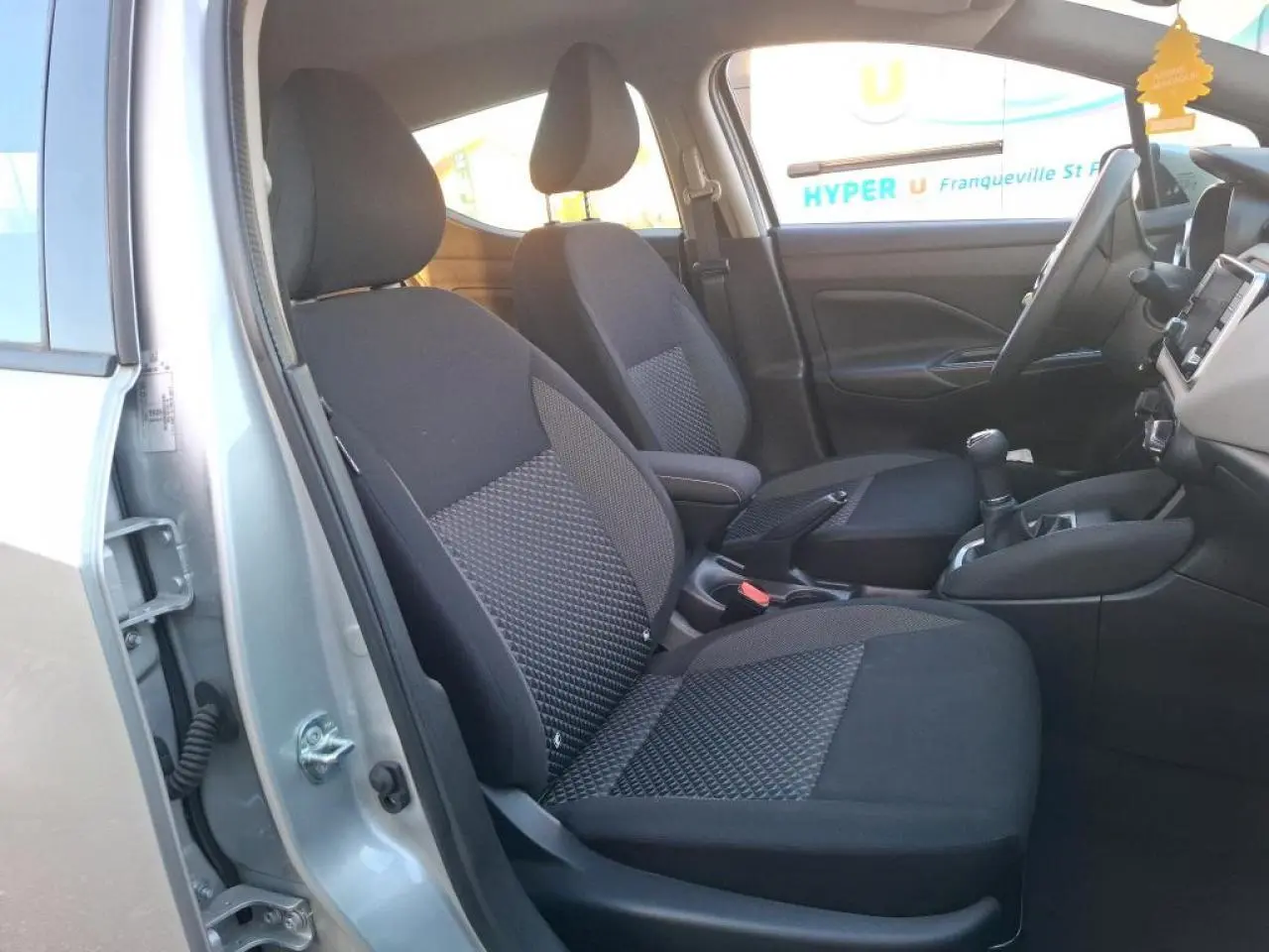 Vue intérieure côté gauche de la Nissan Micra gris clair 2022, montrant les sièges avant en tissu noir et la console centrale.