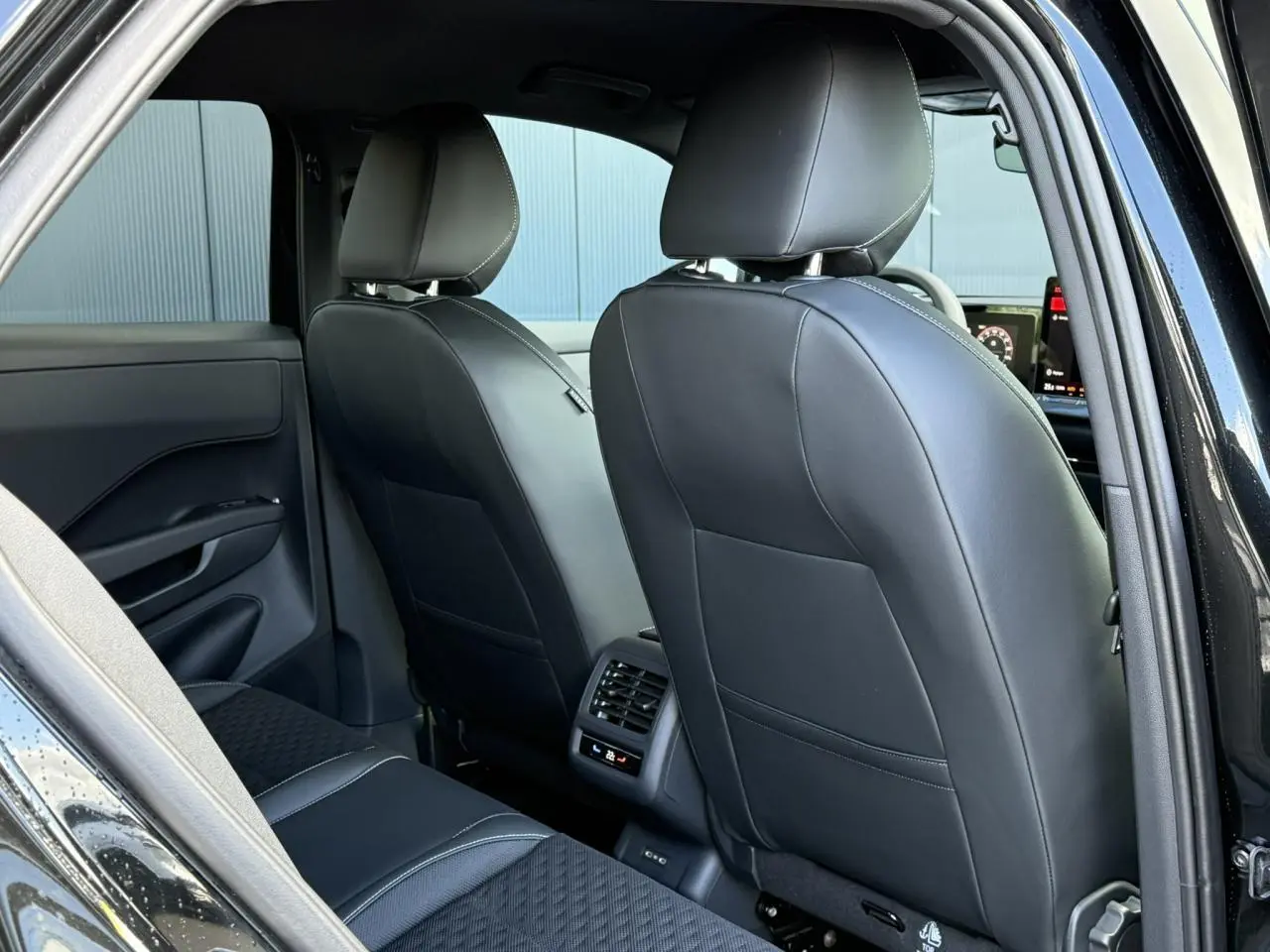 Vue arrière intérieure du Volkswagen T-Roc noir Ébène, montrant les sièges avant en cuir et la console avec ventilation arrière.