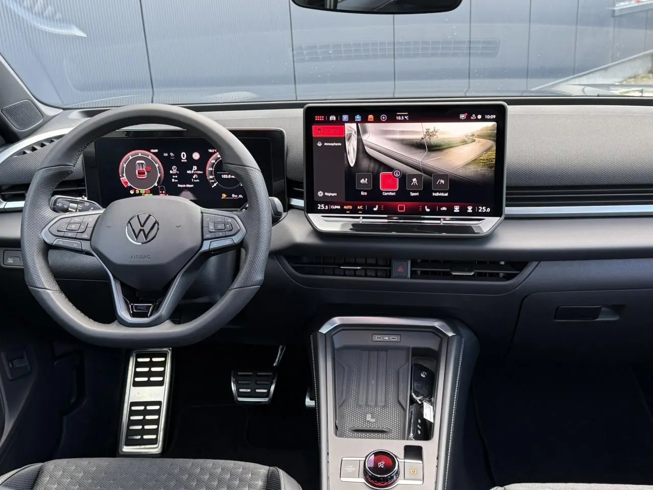Vue frontale de l'habitacle du Volkswagen T-Roc 2026 avec volant multifonction, écran tactile et pédalier sport en acier inox.