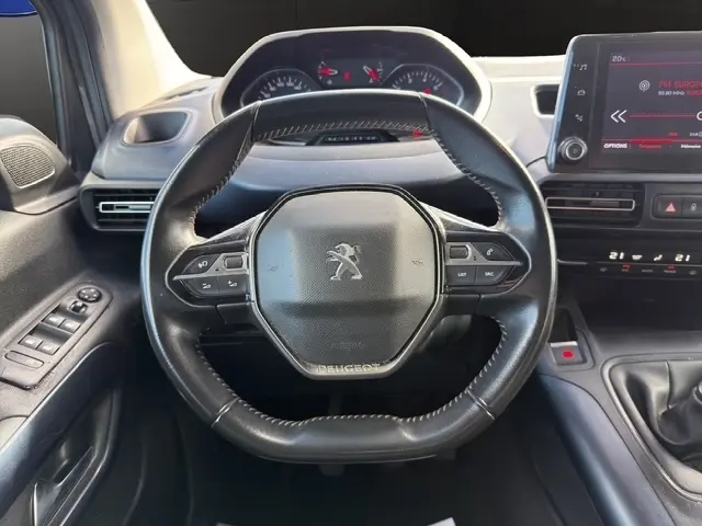 Vue rapprochée du volant cuir multifonctions du Peugeot Rifter gris foncé, avec tableau de bord et écran tactile visibles.