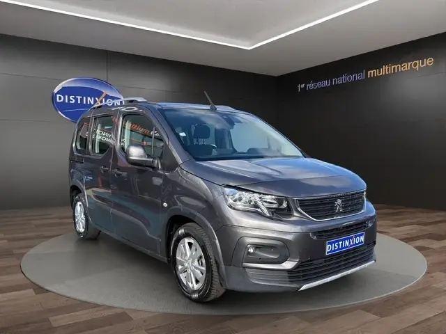Peugeot Rifter BlueHDi 130 gris foncé en 3/4 avant droit, avec calandre noire et jantes argentées visibles.