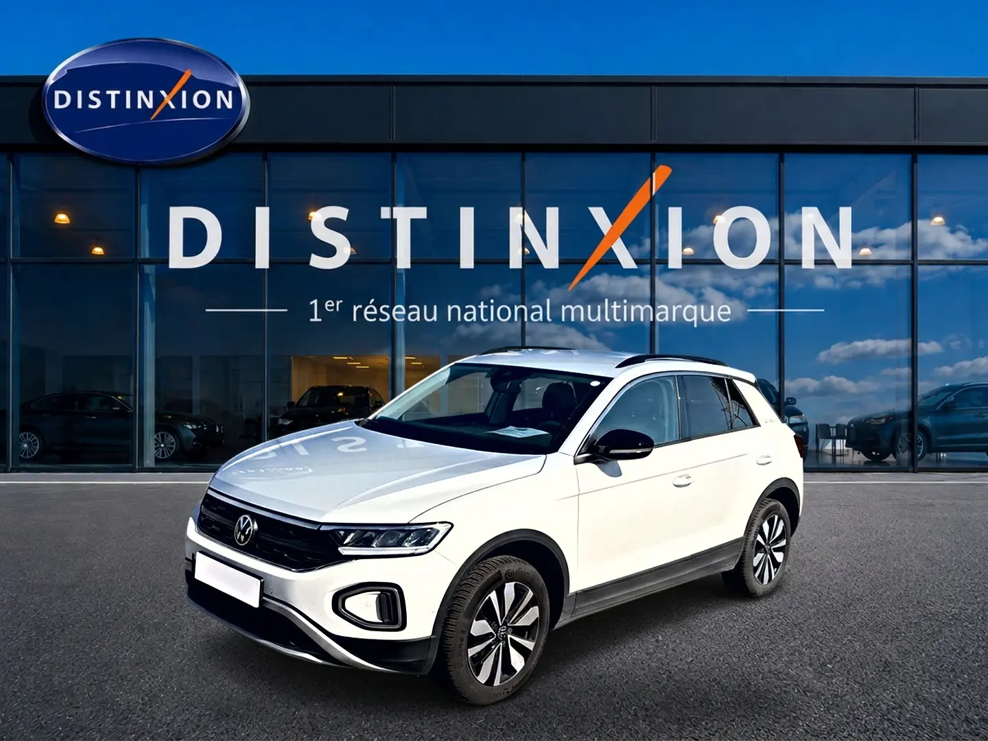 Volkswagen T-Roc blanc en 3/4 avant droit, avec jantes alliage et barres de toit noires visibles.