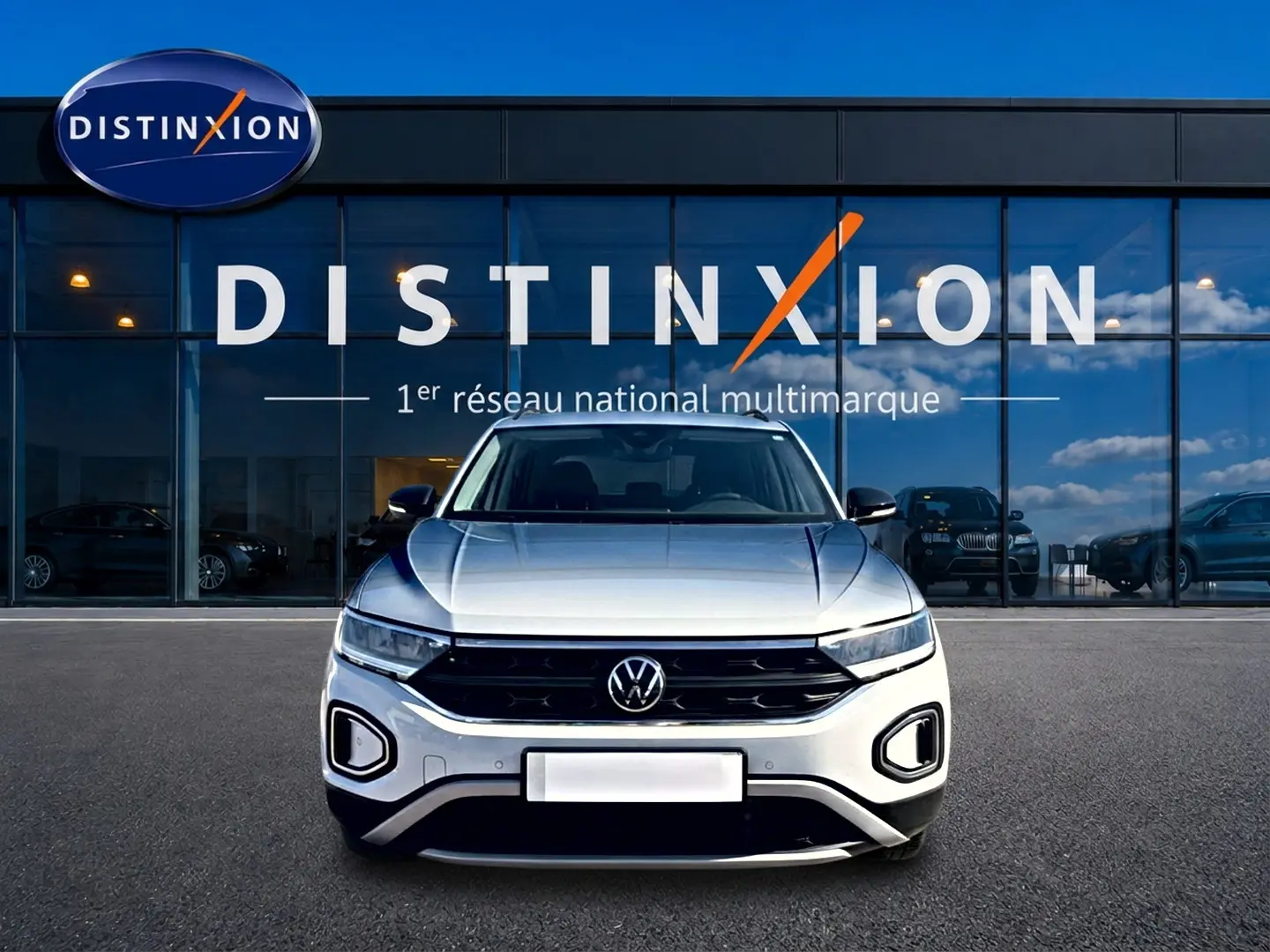 Volkswagen T-Roc blanc vu de face, avec calandre noire et phares LED devant un showroom Distinxion.