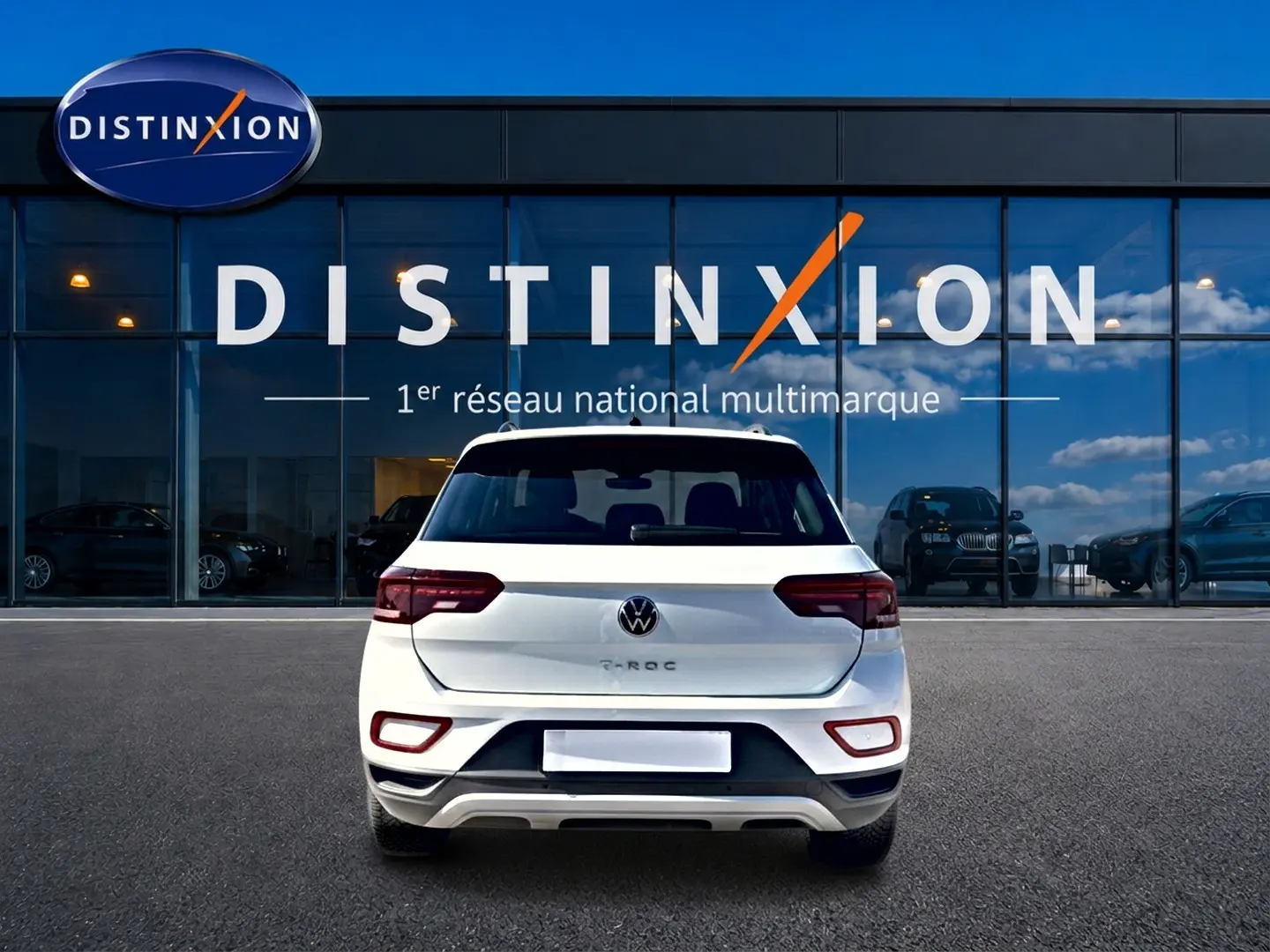 Vue arrière d'un Volkswagen T-Roc blanc 2025 garé devant une vitrine avec logo Distinxion.