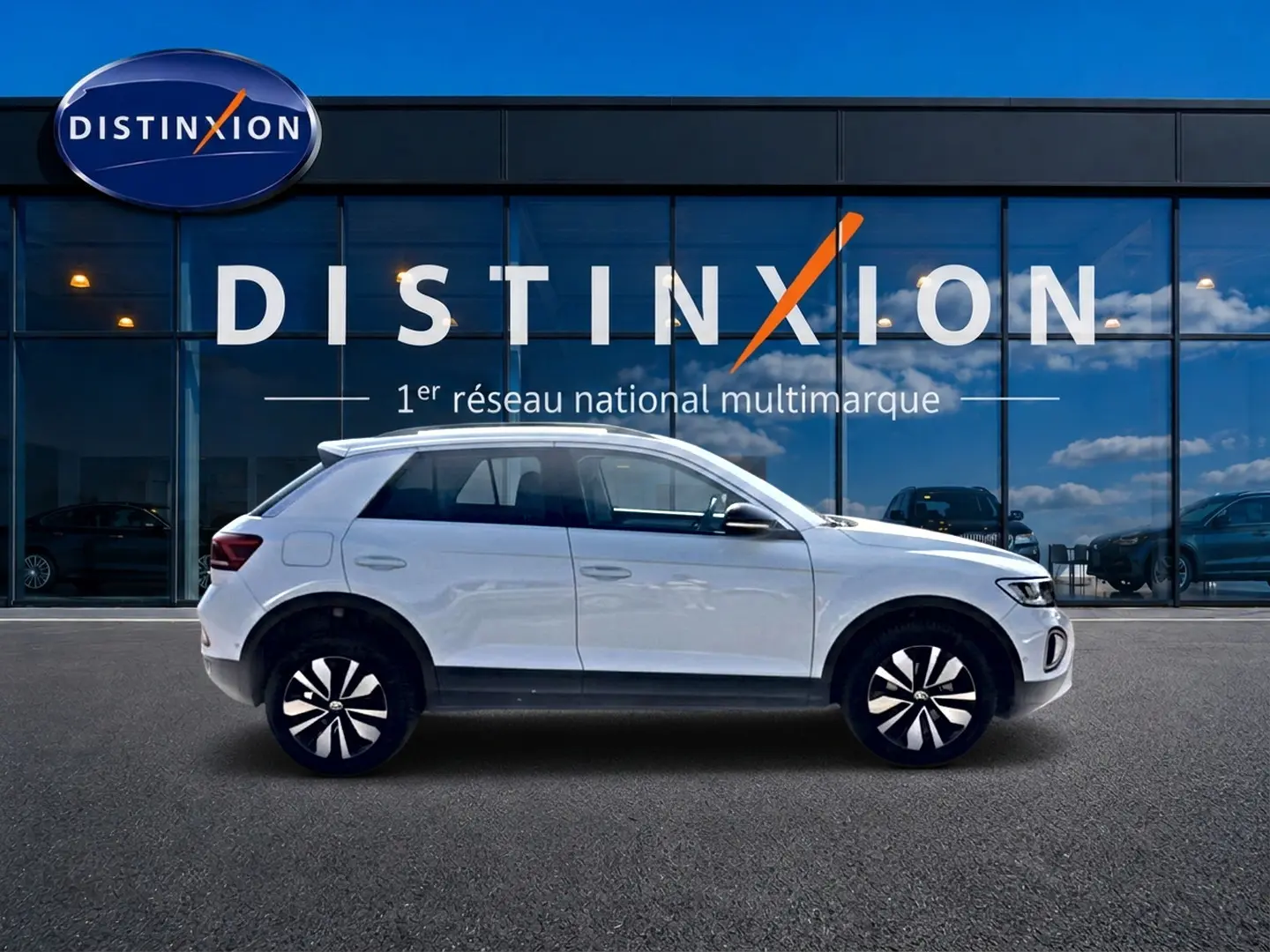 Volkswagen T-Roc blanc en profil droit devant une vitrine avec logo Distinxion visible en arrière-plan.