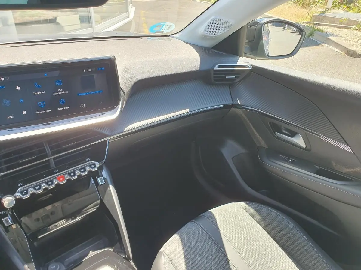 Vue intérieure côté passager de la Peugeot 208 1.2 Hybrid 110 Allure, avec tableau de bord noir et écran tactile 10 pouces.