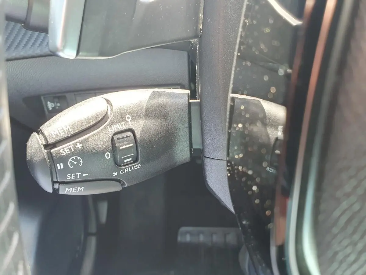 Gros plan sur la commande de régulateur de vitesse à gauche du volant dans une Peugeot 208 gris Artense 2025.