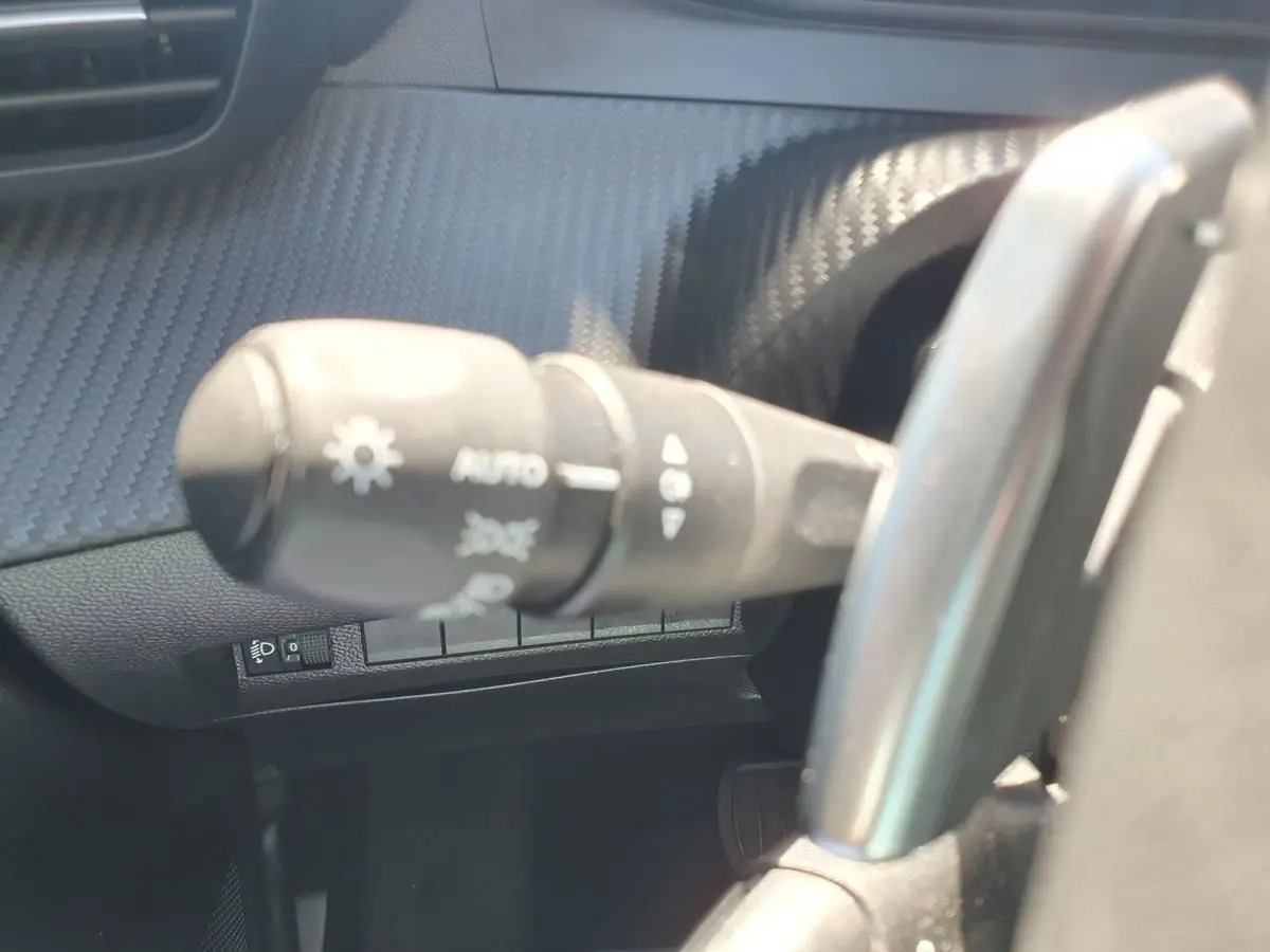 Gros plan sur la commande des feux et clignotants dans l'habitacle d'une Peugeot 208 gris Artense, côté gauche du volant.