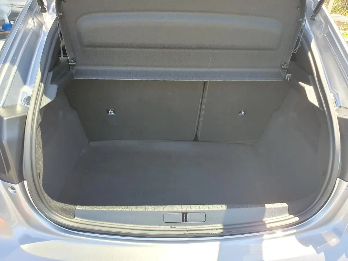 Coffre ouvert vu de l'arrière d'une Peugeot 208 1.2 Hybrid 110 gris Artense, intérieur noir et propre.