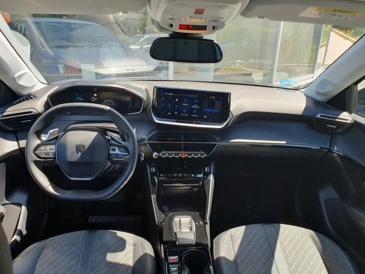 Vue intérieure avant de la Peugeot 208 1.2 Hybrid 110 Allure, tableau de bord moderne avec écran tactile 10'' et volant compact.