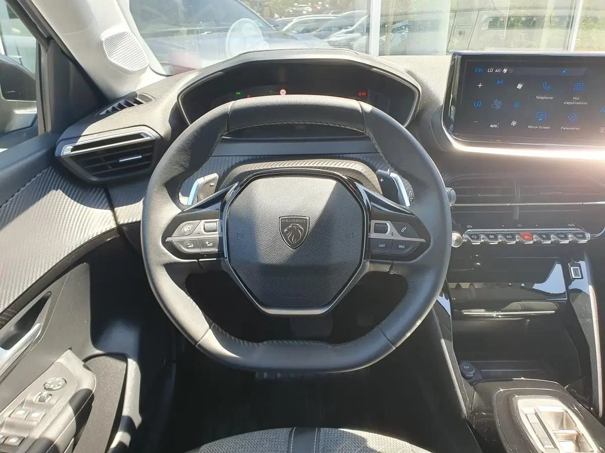 Vue intérieure centrée sur le volant noir de la Peugeot 208 1.2 Hybrid 110 Allure avec tableau de bord et écran tactile.