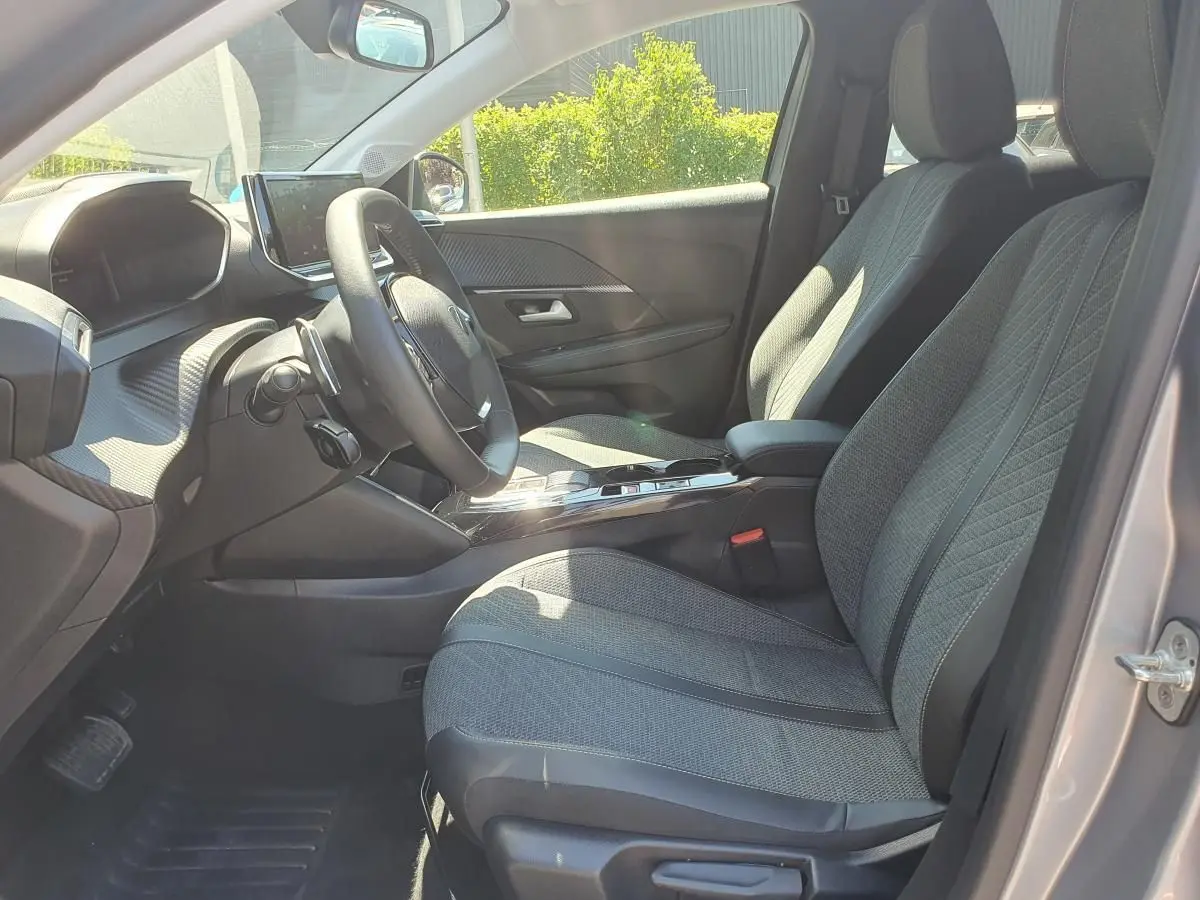 Intérieur de la Peugeot 208 1.2 Hybrid 110 DCS6 Allure vu côté conducteur, sièges gris et tableau de bord moderne.