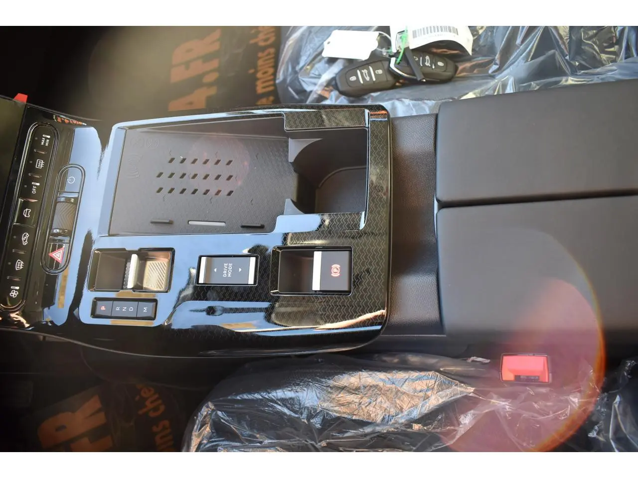 Vue plongeante sur la console centrale noire brillante du Citroën C5 Aircross hybride 2026 avec commandes et porte-clés visibles.