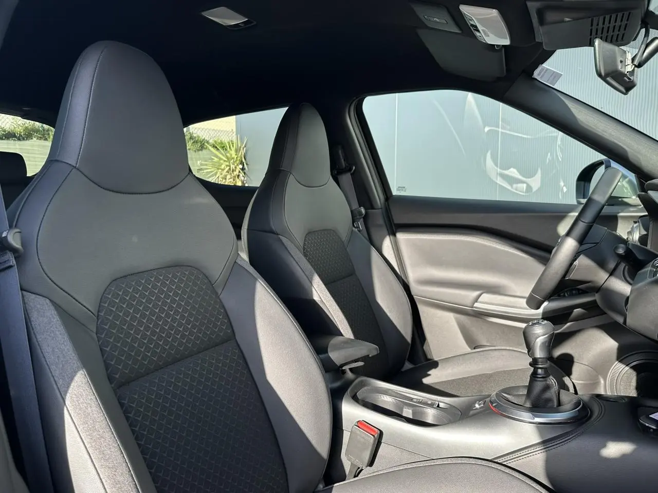Intérieur du Nissan Juke 2025 noir, vue côté droit sur sièges avant en tissu et volant avec boîte manuelle.