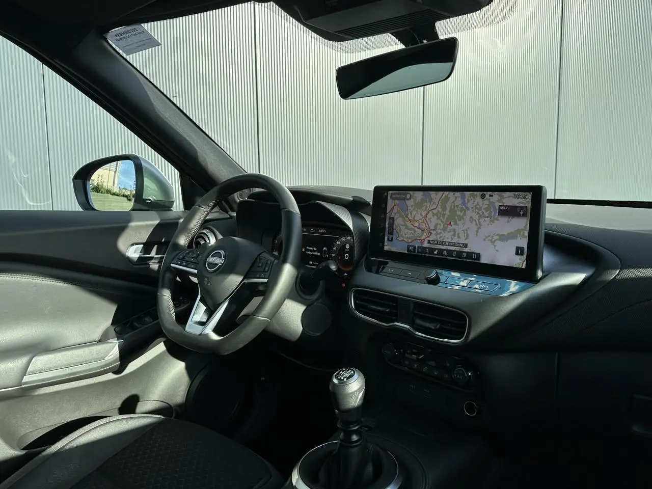 Intérieur du Nissan Juke 2025 noir, vue côté conducteur, tableau de bord avec écran tactile et volant cuir multifonction.