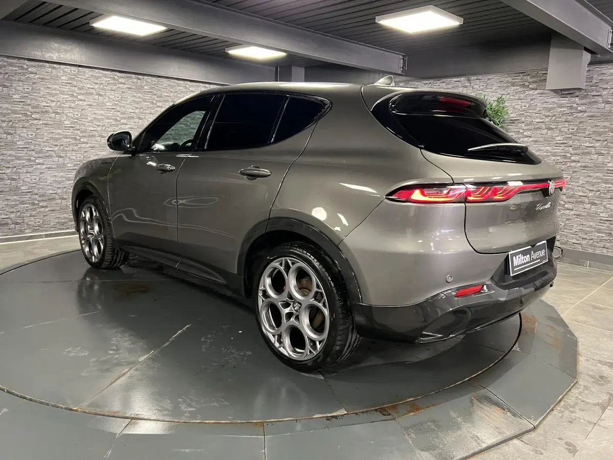 Alfa Romeo Tonale gris foncé vue 3/4 arrière côté gauche, feux arrière allumés et jantes alliage distinctives.