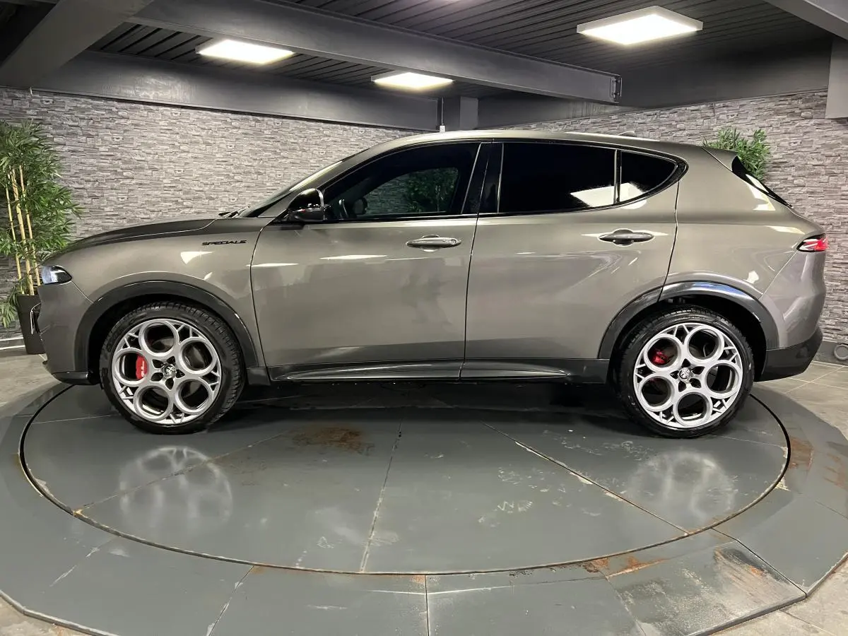 Profil droit d'un Alfa Romeo Tonale gris foncé avec jantes alliage 20 pouces et étriers de frein rouges dans un showroom.