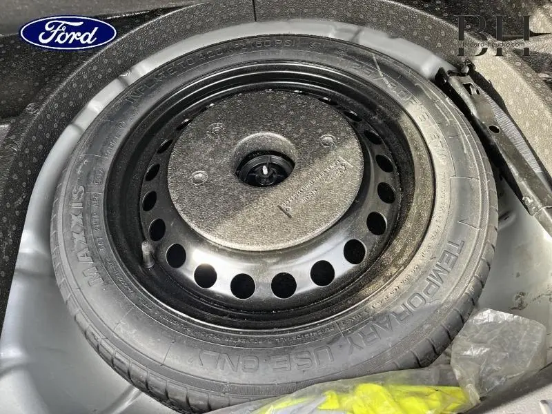Gros plan sur la roue de secours noire dans le coffre du Ford C-MAX gris lunaire, montrant le pneu temporaire et son emplacement.
