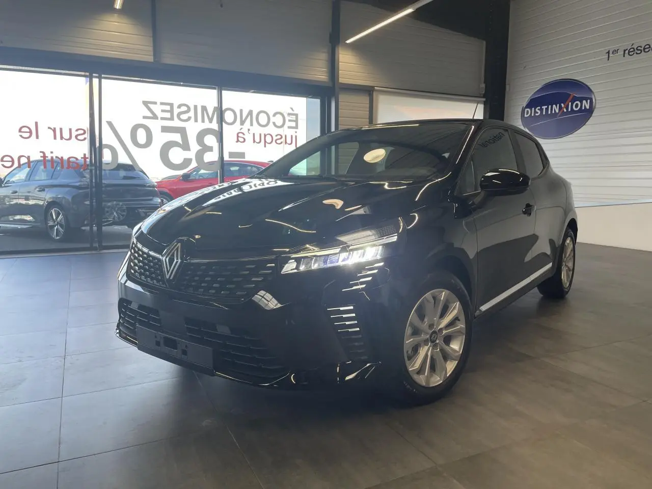 Renault Clio 2025 noir étoilé vue 3/4 avant droit en showroom avec jantes alu et feux LED allumés.