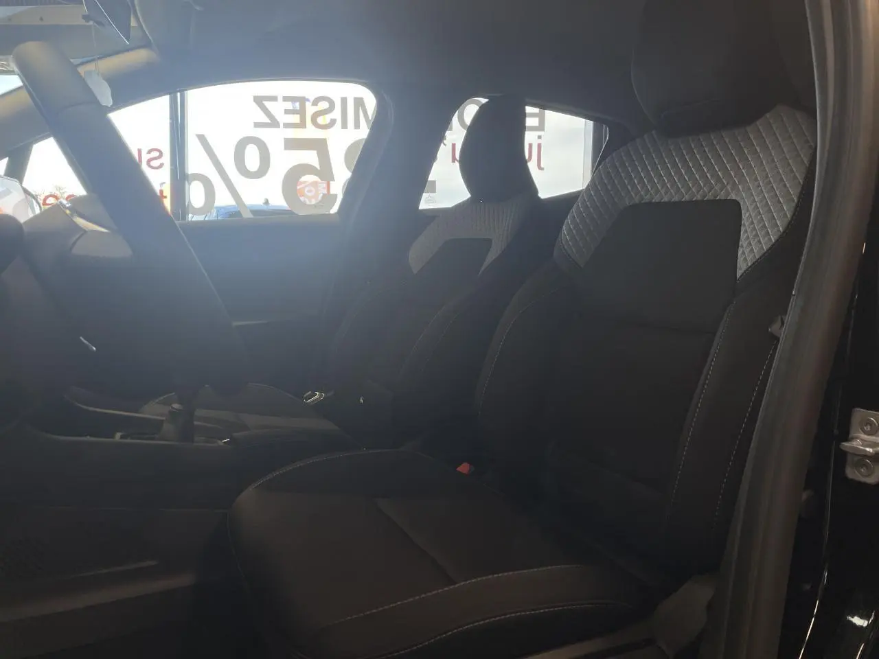 Vue intérieure côté gauche montrant les sièges avant tissu gris et noir de la Renault Clio 1.5 Blue dCi 2025.