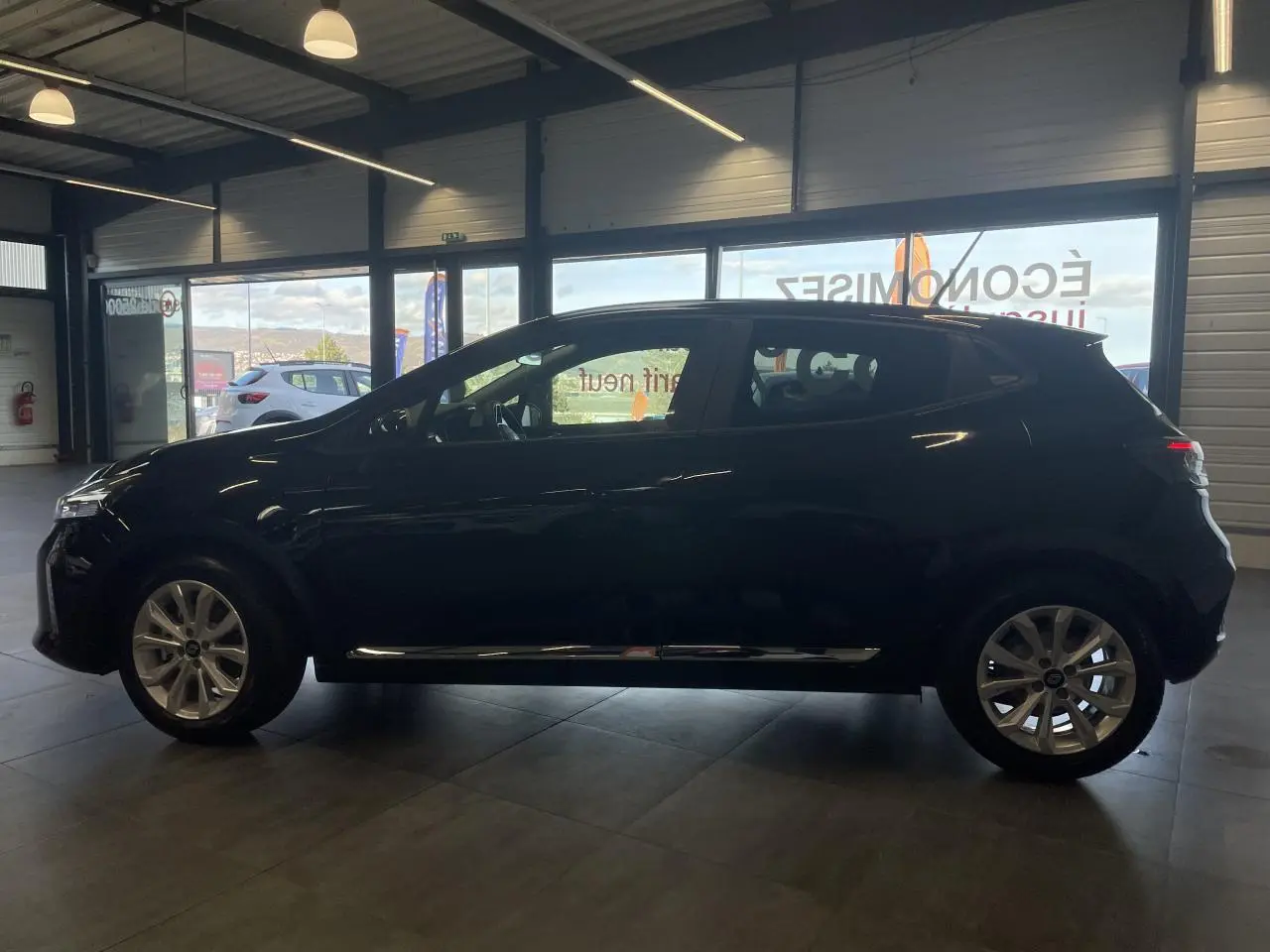 Profil latéral droit d'une Renault Clio 1.5 Blue dCi 2025 en noir étoilé avec jantes alliage en intérieur showroom.