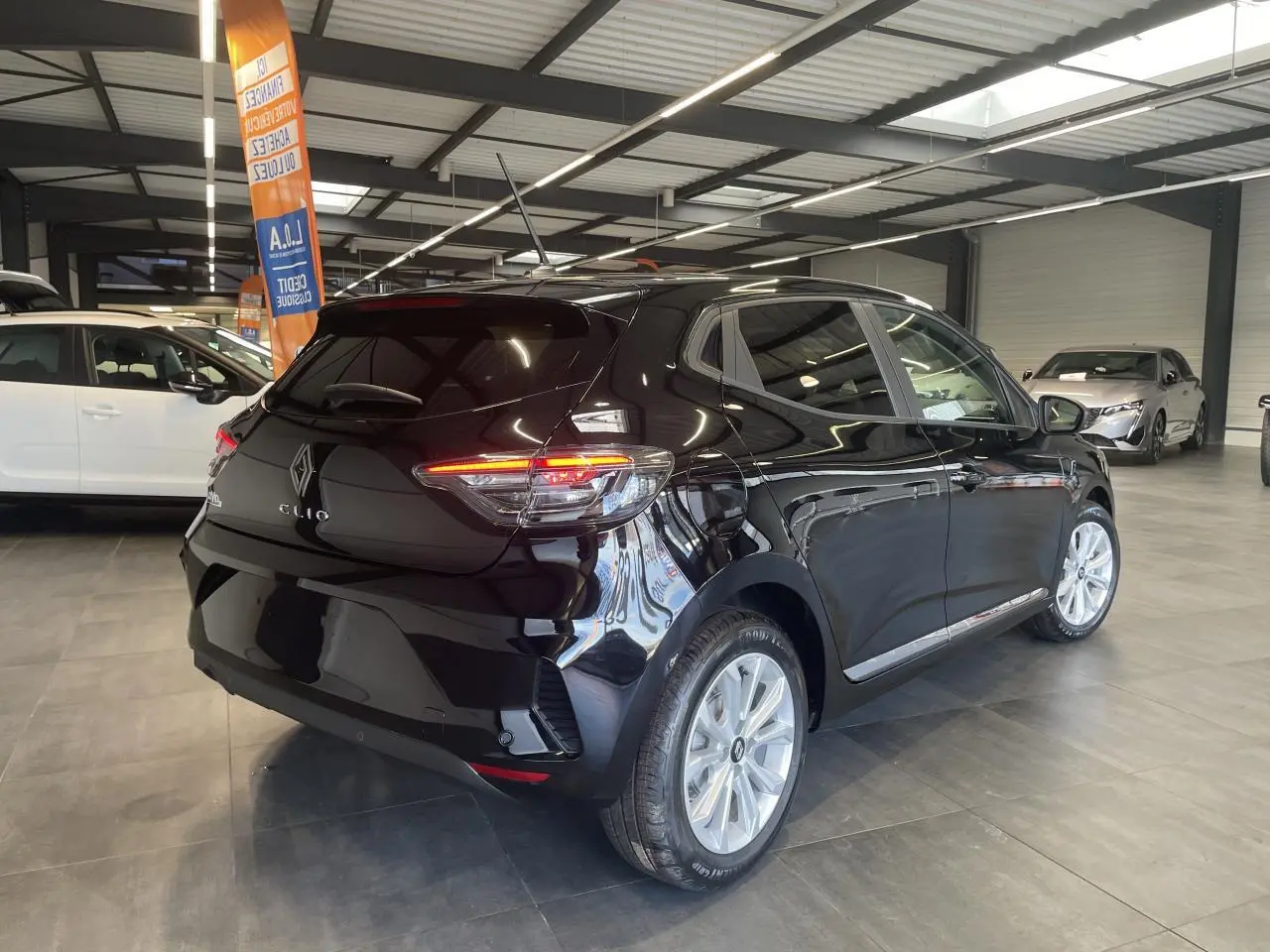 Renault Clio 2025 noir étoilé vue 3/4 arrière droit en intérieur avec jantes alu et feux LED allumés.