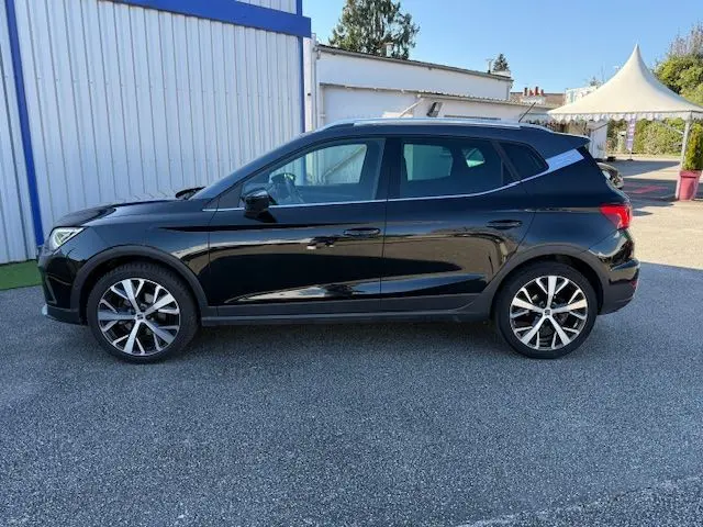 Vue de profil côté gauche d'un SEAT Arona noir avec toit gris, jantes alliage 18 pouces, sur un parking extérieur.