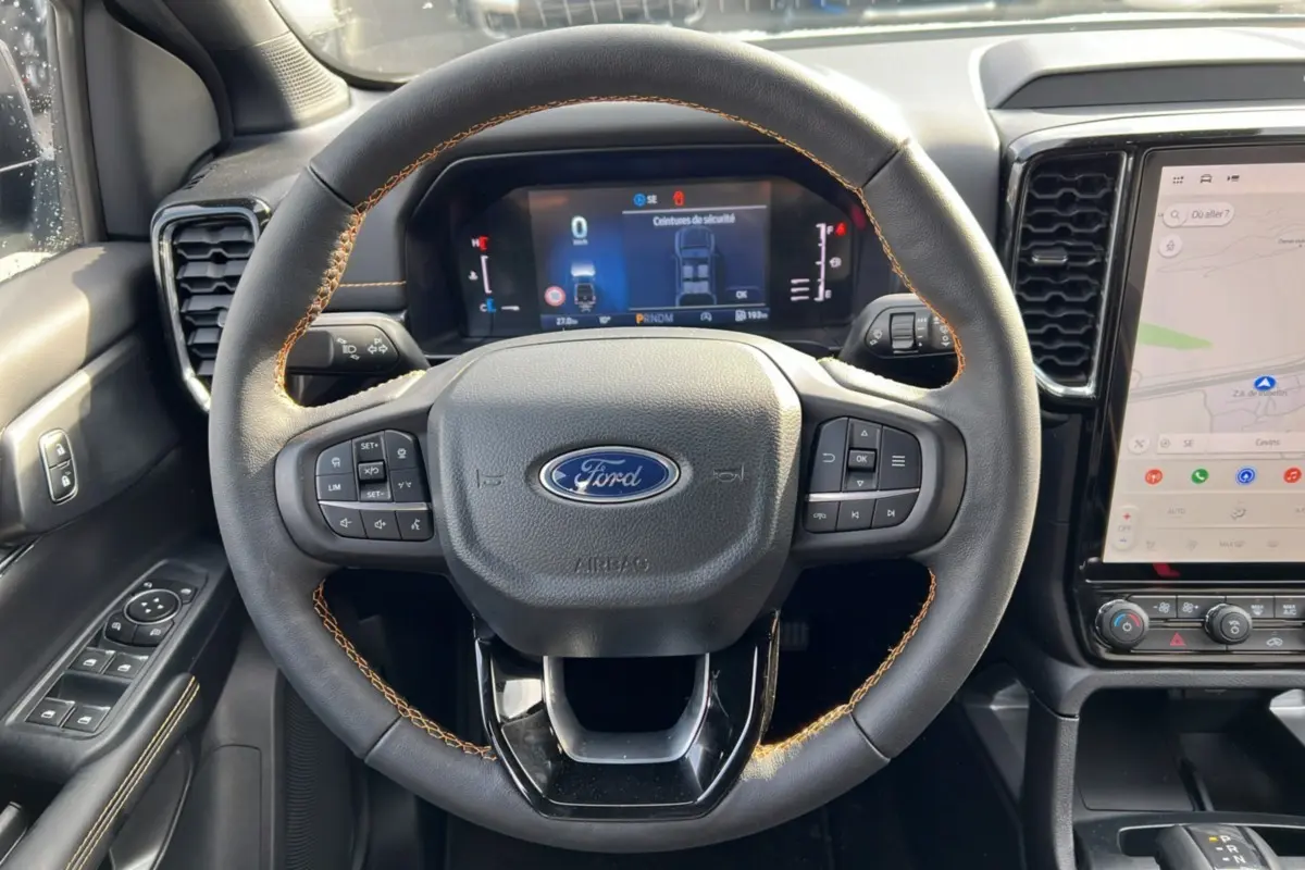 Vue rapprochée du volant cuir noir avec surpiqûres marron du Ford Ranger 2026, tableau de bord digital et écran tactile GPS.