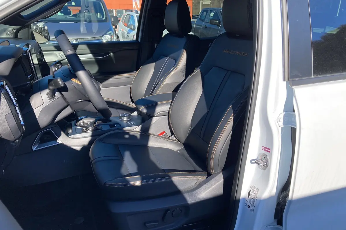 Vue intérieure côté conducteur du Ford Ranger blanc glacier 2026, sièges cuir noirs avec surpiqûres orange Wildtrak visibles.