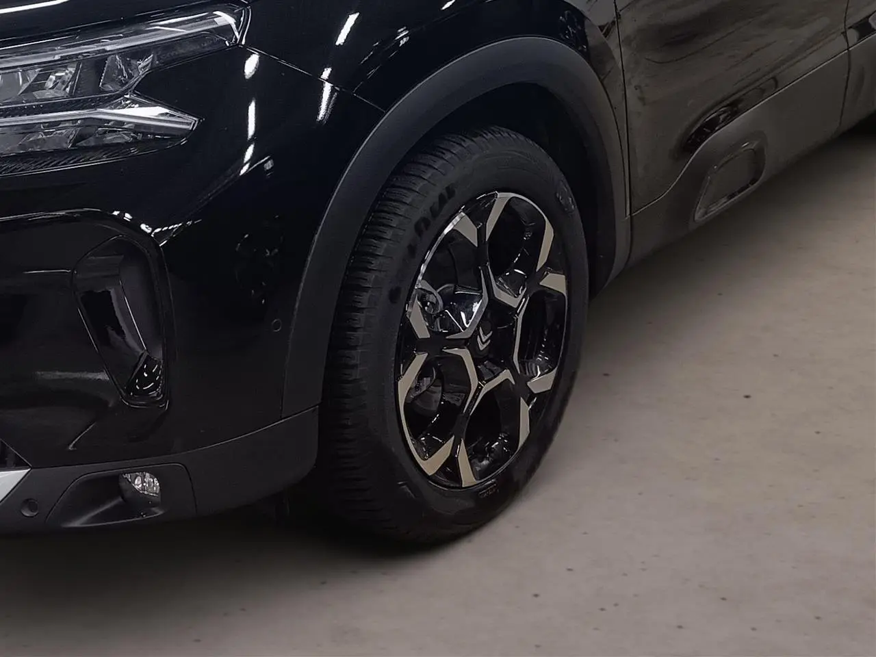 Gros plan sur la roue avant gauche et le pare-chocs noir Perla du Citroën C5 Aircross Hybrid 2025.