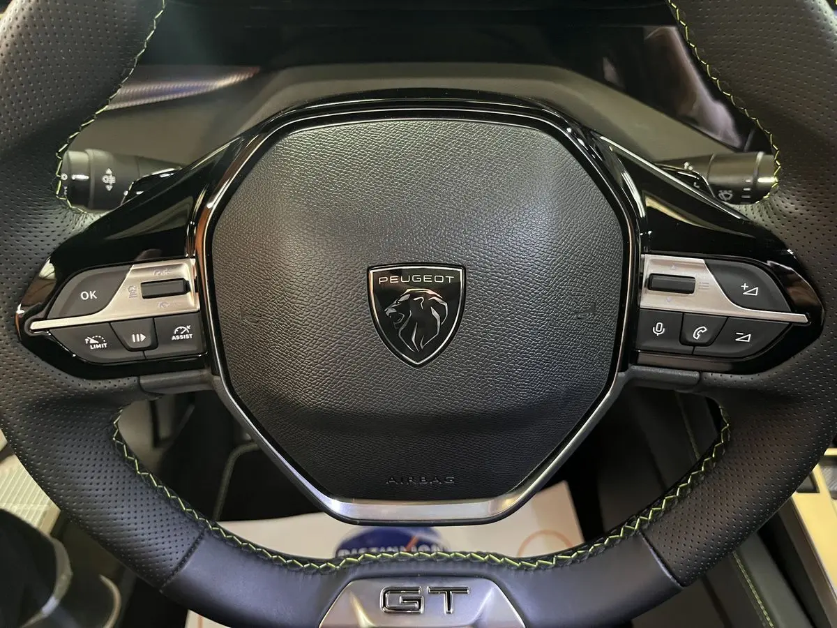 Gros plan sur le volant cuir noir perforé avec surpiqûres vertes et logo Peugeot du 308 GT PHEV 180 Hybride Rechargeable.