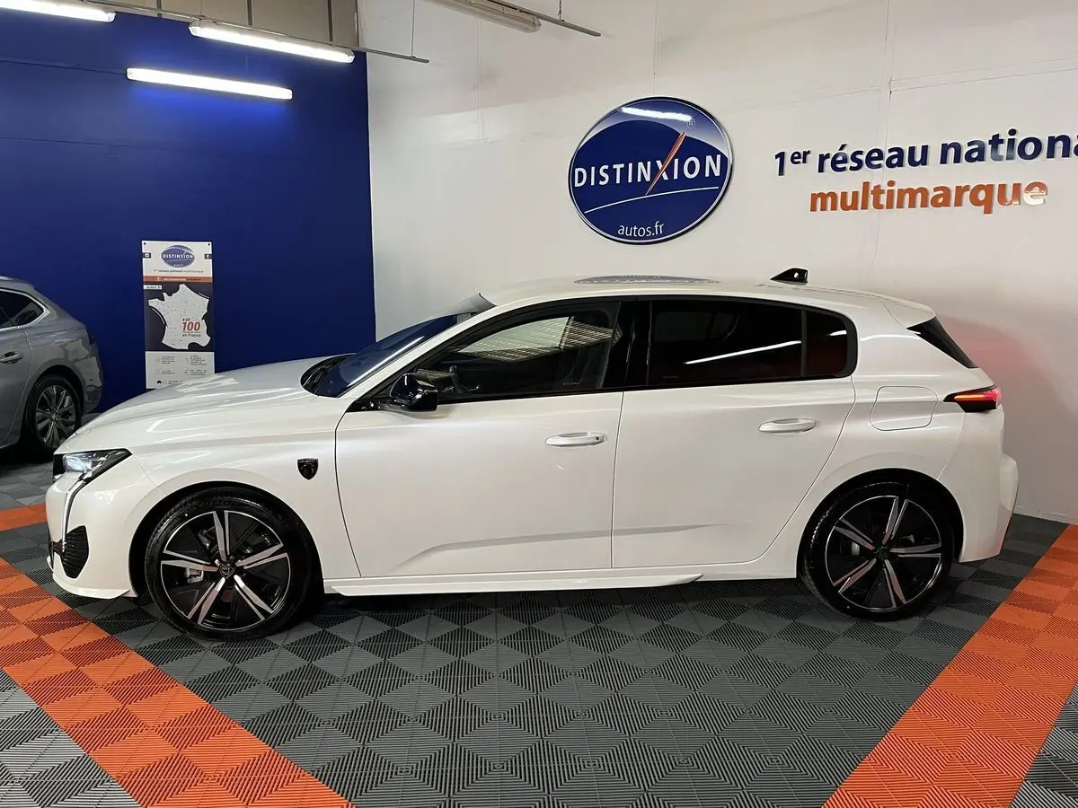 Profil côté gauche de la Peugeot 308 GT PHEV blanche nacrée en hybride rechargeable, avec jantes noires et détails sportifs visibles.