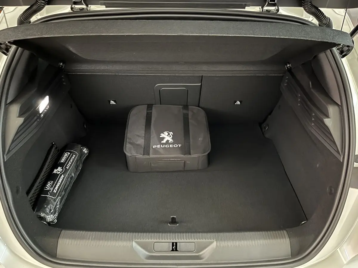 Coffre ouvert d'une Peugeot 308 GT PHEV blanc nacré, montrant un sac Peugeot et un kit d'assistance rangés.