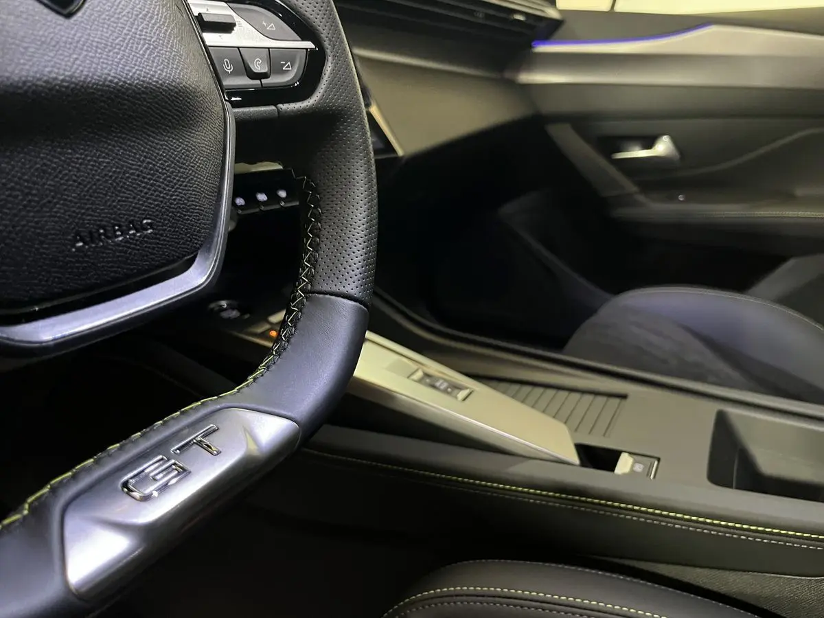 Gros plan sur le volant GT et la console centrale noire avec surpiqûres vertes d'une Peugeot 308 GT PHEV 2022.