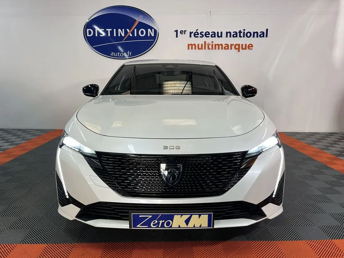 Vue frontale d'une Peugeot 308 GT PHEV blanche nacrée avec calandre noire et phares LED allumés.