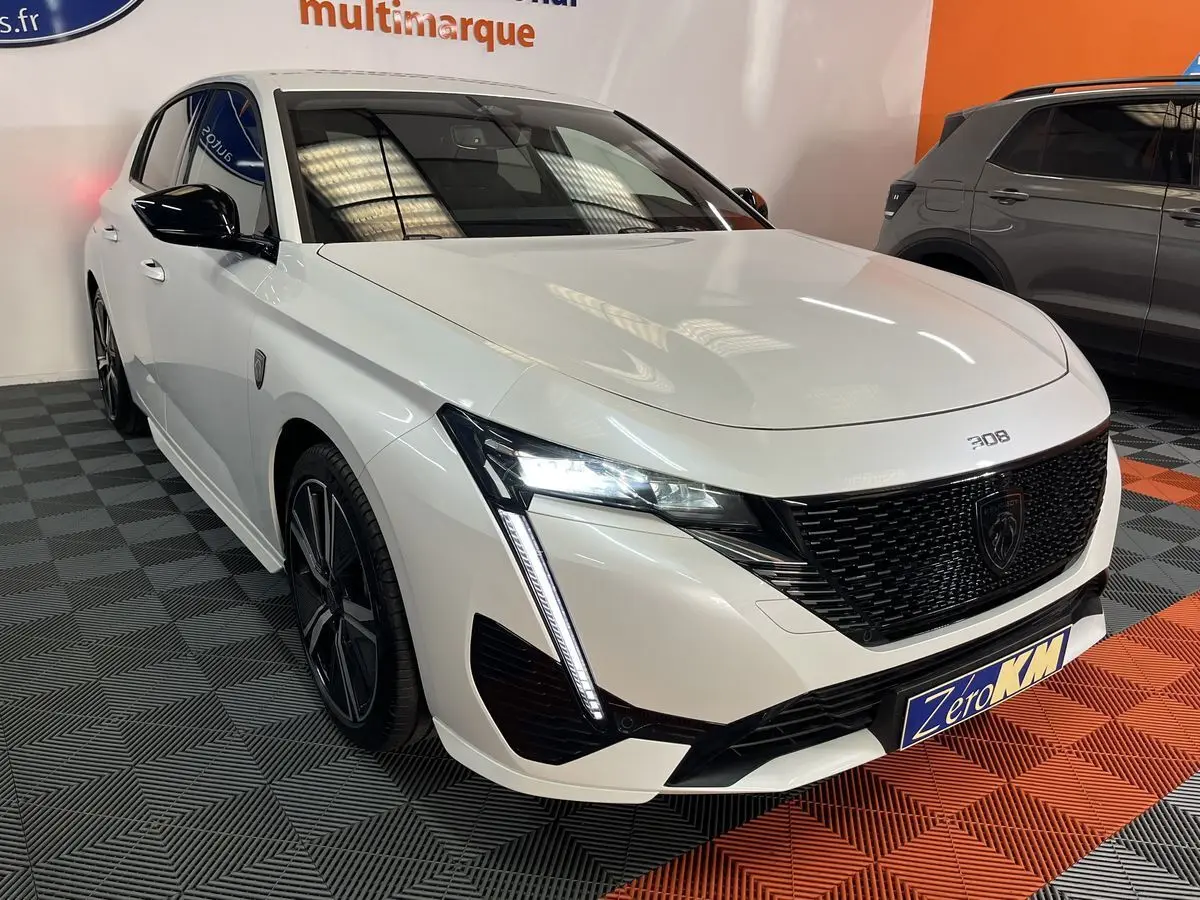 Peugeot 308 GT PHEV blanc nacré vue 3/4 avant gauche avec calandre noire et feux LED en intérieur showroom.