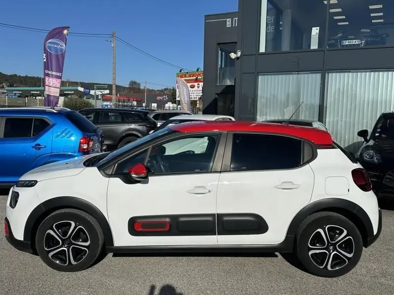 Profil côté gauche d'une Citroën C3 1.2 PureTech 110 Feel Pack blanche avec toit et rétroviseurs rouges, en extérieur.