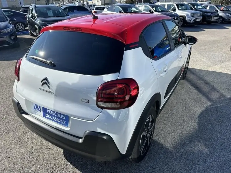 Vue 3/4 arrière droite d'une Citroën C3 blanche avec toit rouge, feux arrière foncés et jantes stylisées.