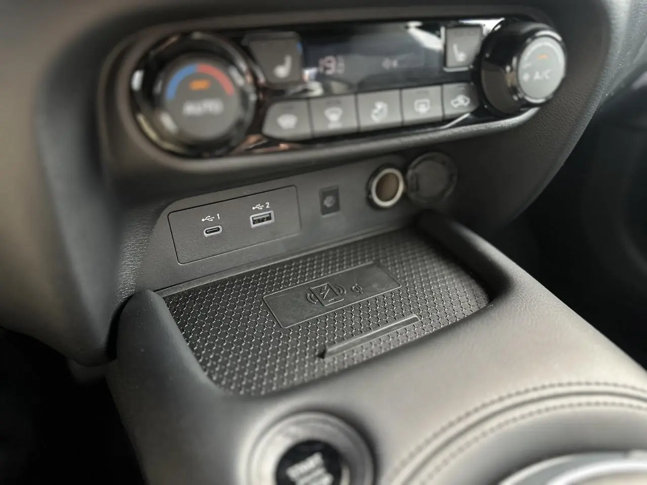 Gros plan sur la console centrale du Nissan Juke 2025, montrant les ports USB, prise 12V et zone de charge sans fil.