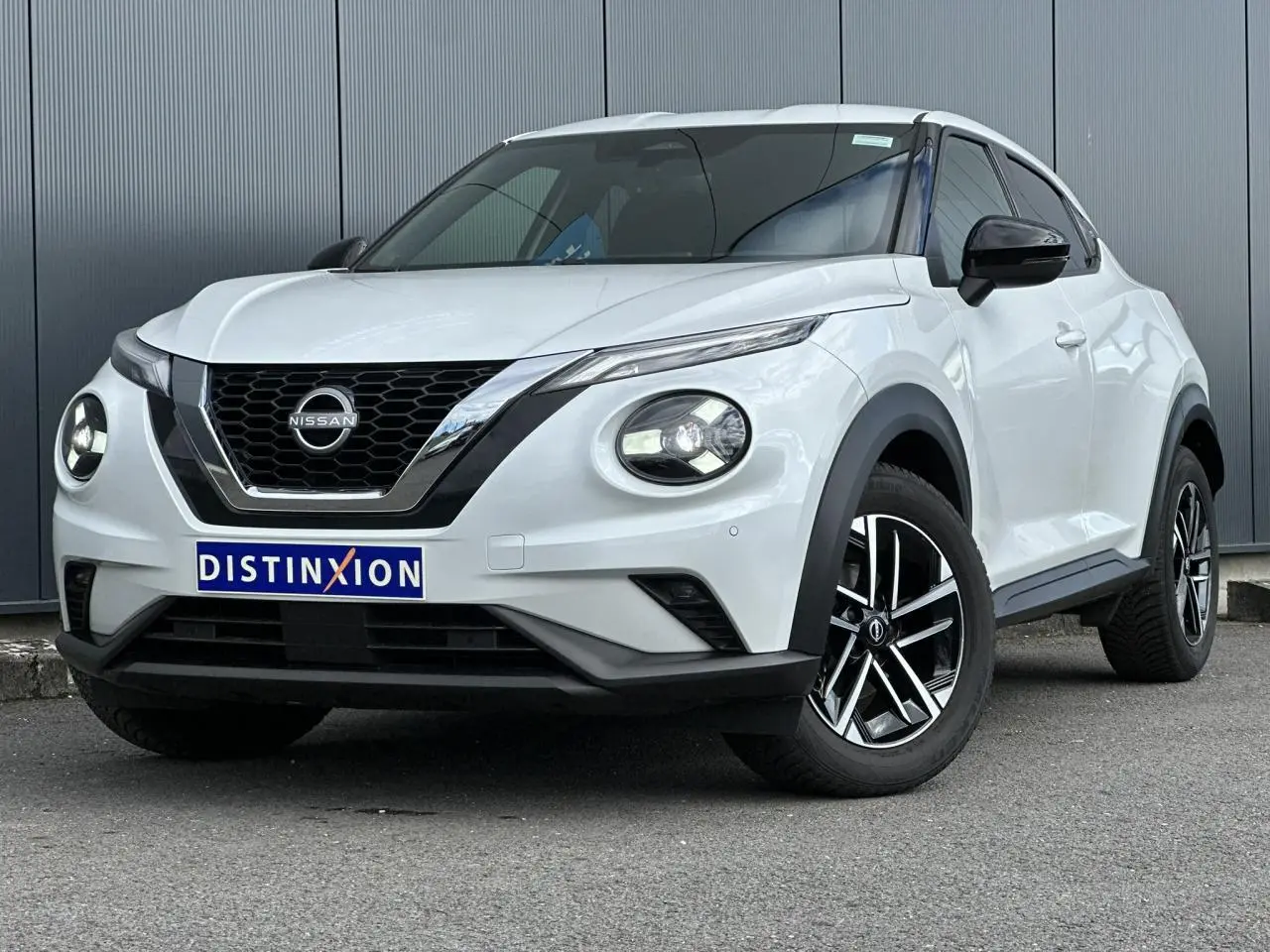 Nissan Juke blanc nacré en 3/4 avant droit, avec calandre chromée et jantes alliage noires et argentées.