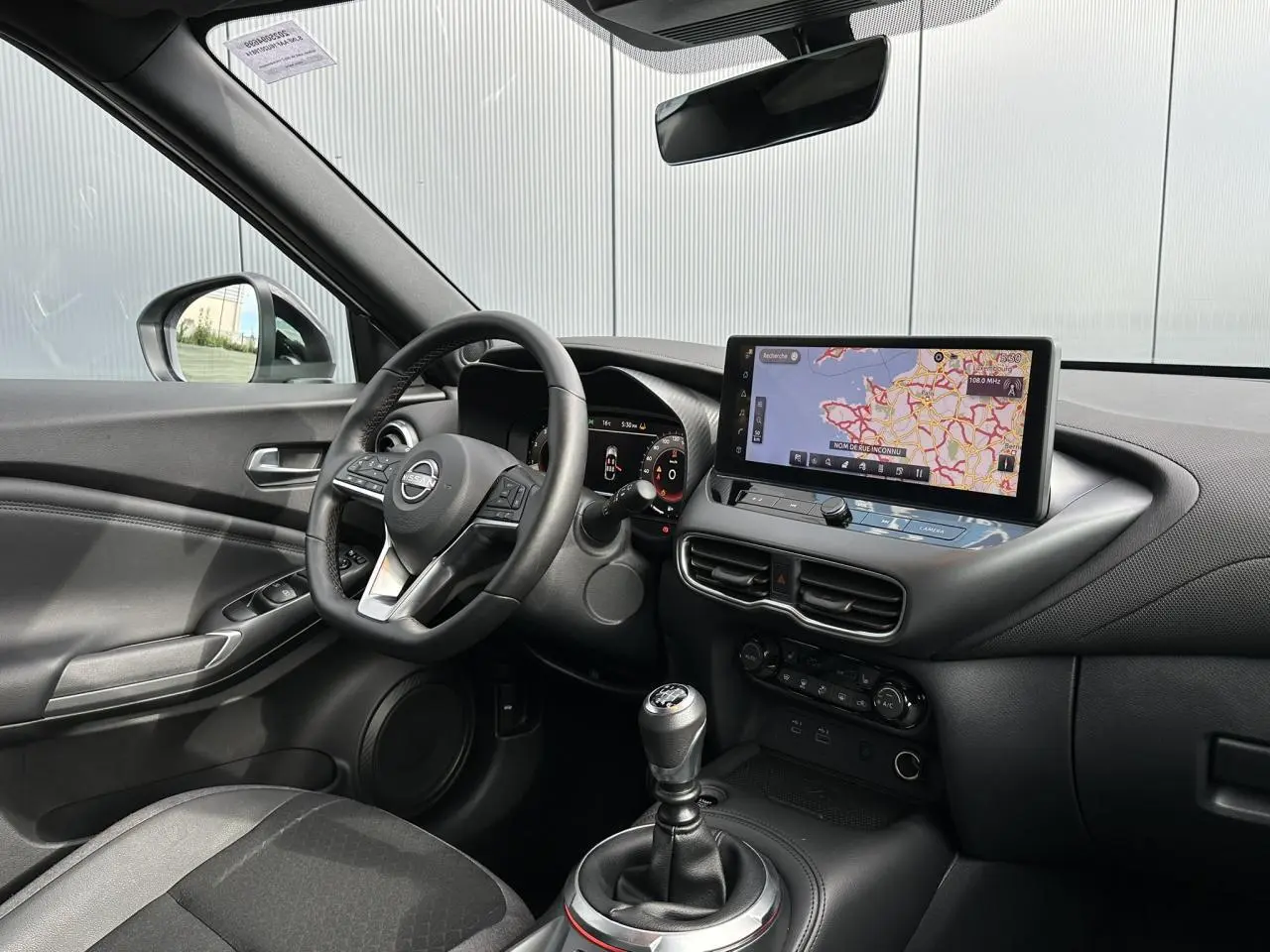 Intérieur noir du Nissan Juke 2025 vu côté conducteur, avec tableau de bord digital et écran tactile GPS.